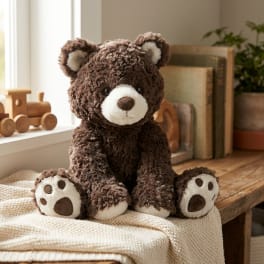 Brown teddy bear plush sitting on a cream knit blanket
