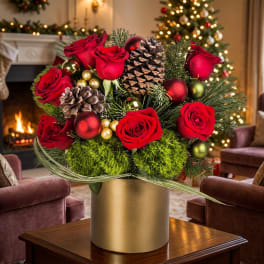 Red roses and pinecones arranged in a gold vase with holiday ornaments