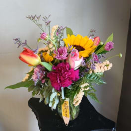 Mixed bouquet with a sunflower, tulips, roses, and pink carnations in a glass vase