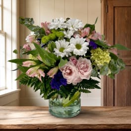 Mixed bouquet of white daisies, pink blooms, and purple accents in a glass vase