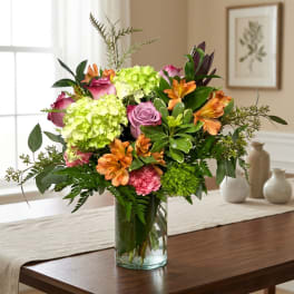 Bouquet of pink roses, green hydrangeas, and orange lilies in a glass vase