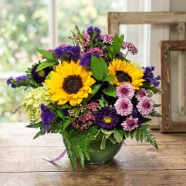 Bouquet with sunflowers, purple blooms, and pink flowers in a green vase
