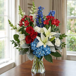 Bouquet of red roses, white lilies, blue hydrangeas, and snapdragons in a glass vase