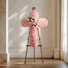 Pink floral cross arrangement on a stand with a ribbon bow