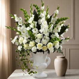 Tall white floral arrangement in a white urn vase with green accents
