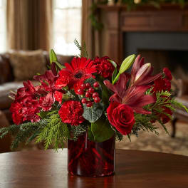 Red floral arrangement in a red glass vase with lilies, roses, and carnations