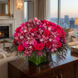 Pink roses and orchids arranged in a square glass vase