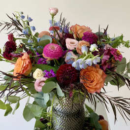 Mixed bouquet of orange, pink, and purple flowers in a textured vase
