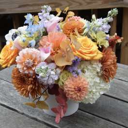 Mixed bouquet of orange, pink, white, and lavender flowers in a white vase