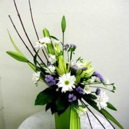 Tall floral arrangement with white daisies and purple blooms in a green vase