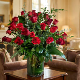 Red roses arranged in a clear glass vase with greenery