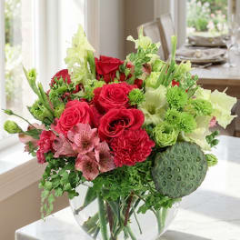 Bouquet of red roses, pink alstroemeria, and green flowers in a clear glass vase