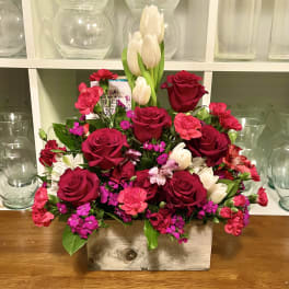 Mixed bouquet of red roses, pink carnations, and white tulips in a rectangular vase