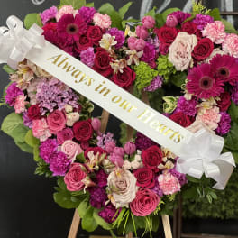Heart-shaped floral wreath with pink and red roses and a white ribbon