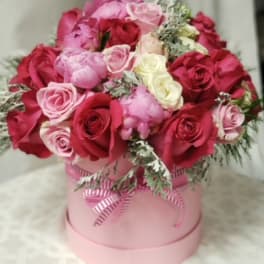 Pink and red roses arranged in a round pink box with a ribbon