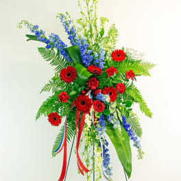 Standing floral spray with red gerberas and blue flowers on a metal easel
