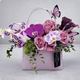 Pink and purple flowers arranged in a lavender gift bag with butterfly decorations