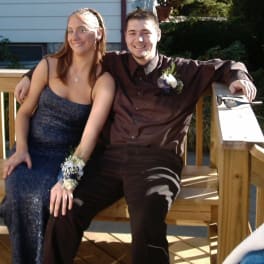 Young couple seated outdoors, each wearing a floral corsage or boutonniere