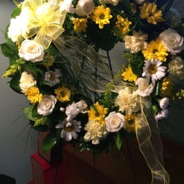 Heart-shaped floral wreath with white roses and yellow daisies on a stand