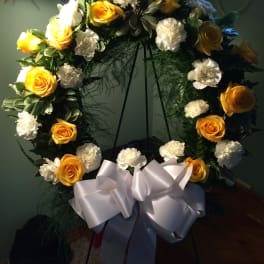Yellow roses and white carnations arranged in a wreath with a white bow