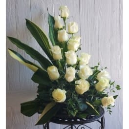 Tall arrangement of white roses with broad dark green leaves
