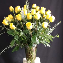 Yellow roses arranged in a clear glass vase with eucalyptus foliage