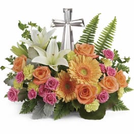 Floral arrangement with white lilies, roses, gerbera daisies, and a silver cross