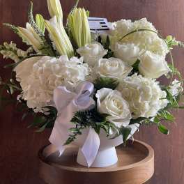 White floral arrangement in a pedestal vase with a lavender ribbon