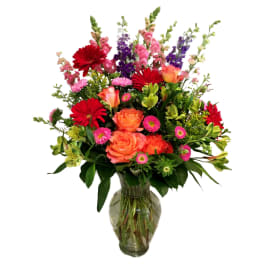Mixed bouquet of roses, gerbera daisies, and purple spikes in a glass vase