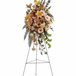 Tall floral standing spray on an easel with yellow and peach flowers