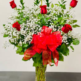Red roses and white baby's breath in a clear glass vase with a red bow