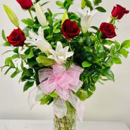 Red roses and white lilies in a clear glass vase with a pink bow
