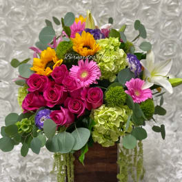 Mixed bouquet with pink roses, sunflowers, lilies, and green hydrangeas in a wooden box
