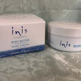 Box and jar of Inis body butter on a patterned fabric surface