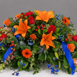 Large floral arrangement with orange lilies, red roses, and blue accents.