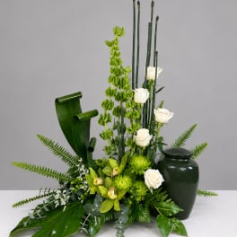 Green floral arrangement with white roses in a dark vase