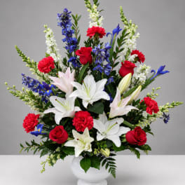 Large mixed bouquet in a white vase with red, white, blue, and pink flowers.