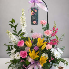Standing floral sympathy arrangement with lilies, roses, and daisies on a black easel