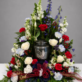 Standing floral tribute with red, white, and blue flowers around an urn