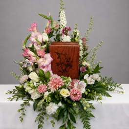 Floral funeral arrangement around a wooden urn with pink and white flowers