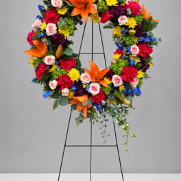 Colorful floral wreath on a black stand with orange lilies and pink roses