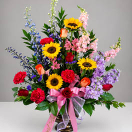 Colorful mixed flower arrangement in a bronze vase with a pink ribbon
