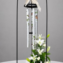 White lilies and roses arranged beneath a black wind chime stand