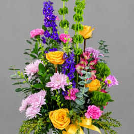 Tall mixed bouquet in a white vase with yellow roses, purple flowers, and pink blooms
