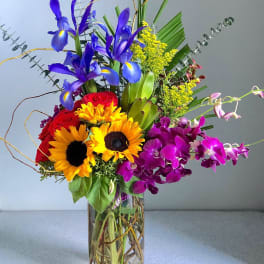 Colorful bouquet with sunflowers, roses, irises, and orchids in a glass vase