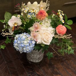 Mixed bouquet in a gray vase with orchids, roses, hydrangea, and small daisies