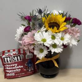 Mixed bouquet in a black vase with a bag of M&M's candy beside it