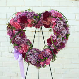 Heart-shaped floral wreath in pink, purple, and lavender tones on a stand