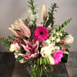 Mixed bouquet of pink lilies, white roses, and bright gerbera daisies in a glass vase