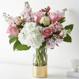 Pink and white flower bouquet in a clear vase with a gold base